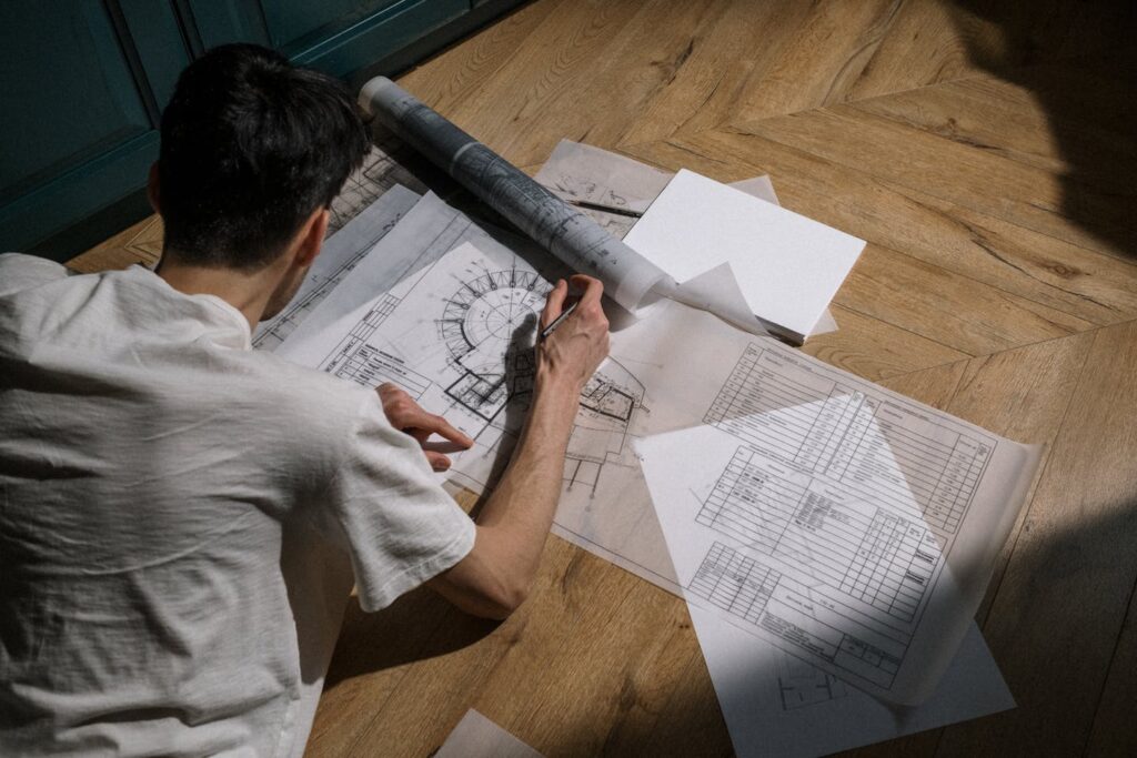 Caucasian man drawing architectural designs on wooden floor with sunlight streaming in.